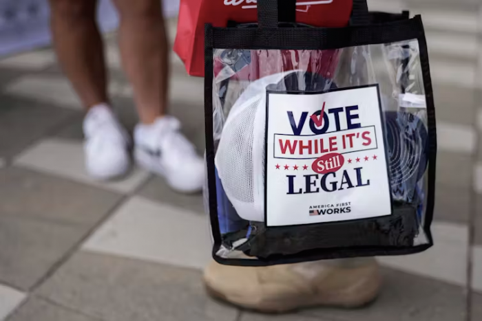 Person holding clear plastic shopping bag with slogan "Vote while it's stilll legal"