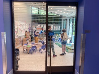 View through glass windows of children and adults in a room with child-sized furniture