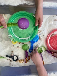 Children's hands are seen playing with various toys in sand.