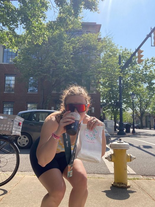 Shelly mugs for the camera while sipping a drink and holding a bag from Call Your Mother deli.