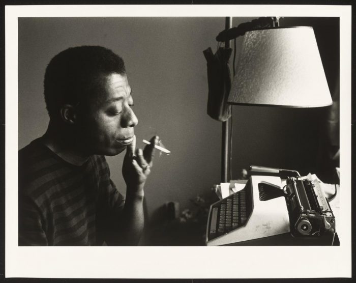 Baldwin smoking a cigarette and contemplating his typewriter