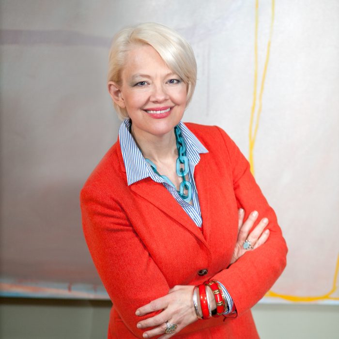 Kim Sajet, wearing orange suit, poses with arms crossed
