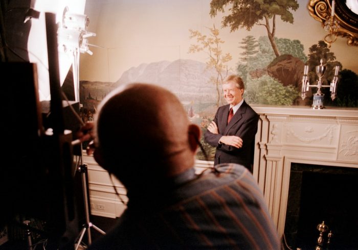 Adams is seen from behind as he photographs Jimmy Carter, standing with his arms crossed.