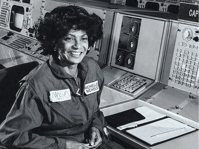 Black and white photo of Nichols in a NASA uniform seated at a control panel