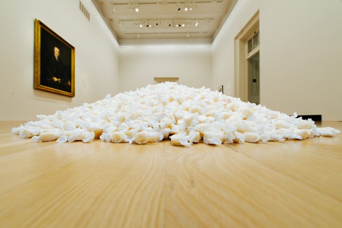 Installation view of whAt appears to be a pile of plastic bags full of white powder piled on gallery floor
