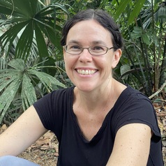 Headshot of Racel Page photographed against tropical foliage