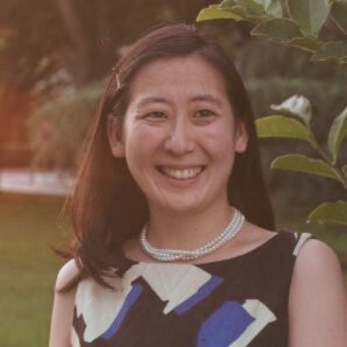 Head shot of Angela Han in print dress and pearls, photographed outdoors